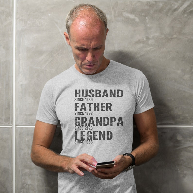 Pode incluir: Uma camiseta cinza com texto preto que diz "Husband since 1989, Father since 1993, Grandpa since 2023, Legend since 1963".