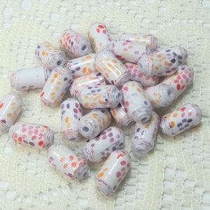 May include: A pile of white, orange and purple polka dot beads. The beads are made of paper and are rolled into a cylinder shape.