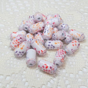 May include: A pile of white paper beads with orange, pink, and purple polka dots. The beads are arranged in a random pattern on a white crocheted surface.