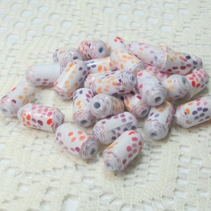 May include: A pile of white paper beads with orange, pink, and purple polka dots. The beads are arranged in a random pattern on a white crocheted surface.