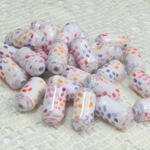 May include: A pile of white ceramic beads with a colourful polka dot pattern. The beads are approximately 2.5 cm long and have a cylindrical shape.