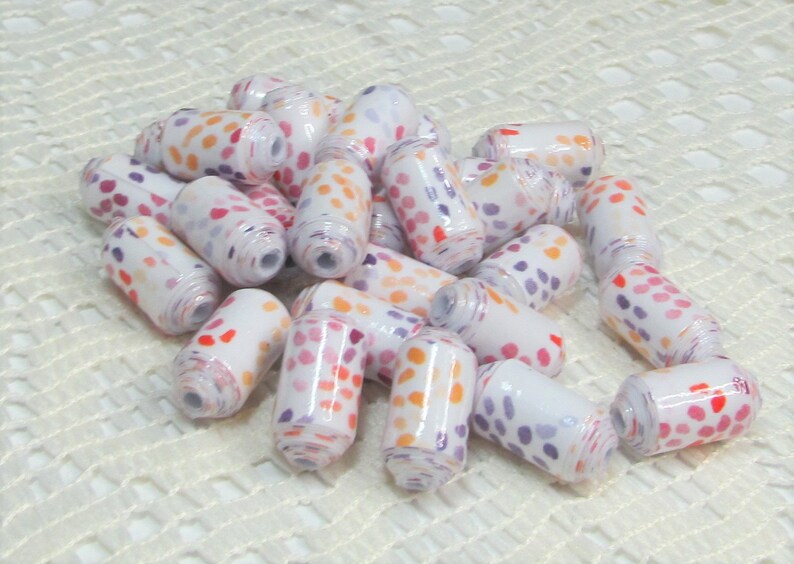 May include: A pile of white ceramic beads with a colourful polka dot pattern. The beads are approximately 2.5 cm long and have a cylindrical shape.