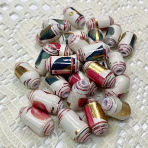 May include: A collection of cylindrical beads featuring a white base with layered paper patterns in shades of red, teal, and metallic gold. Each bead has a central hole and a smooth, glossy finish, showcasing intricate rolled paper textures.