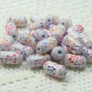 May include: A pile of white cylindrical beads with a colourful polka dot pattern. The beads are made of paper and are perfect for crafting.