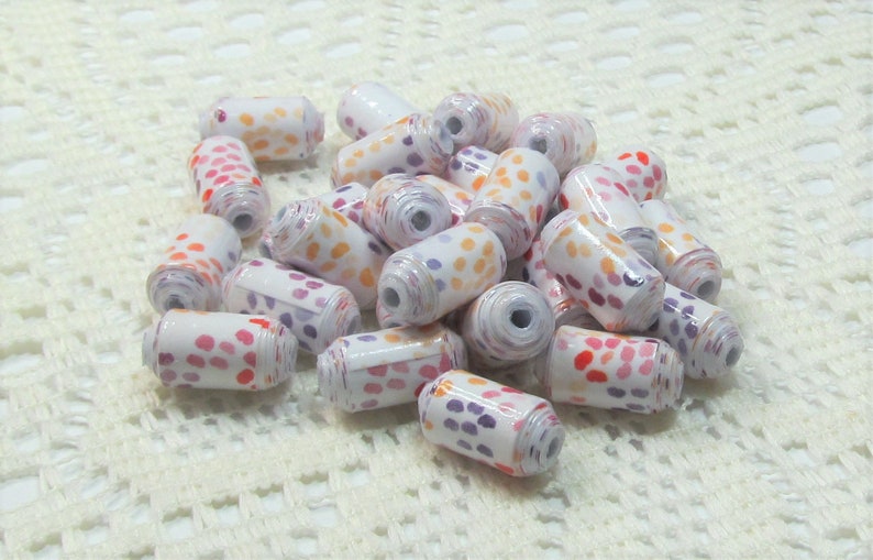 May include: A pile of white cylindrical beads with a colourful polka dot pattern. The beads are made of paper and are perfect for crafting.