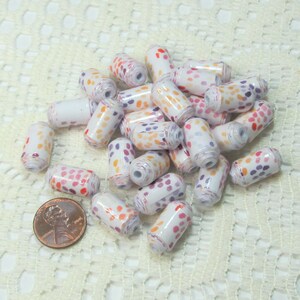May include: A pile of white cylinder beads with orange, pink, and purple polka dots. The beads are about the size of a UK penny.