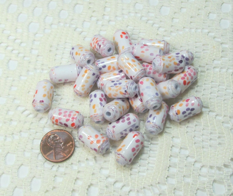 May include: A pile of white cylinder beads with orange, pink, and purple polka dots. The beads are about the size of a UK penny.