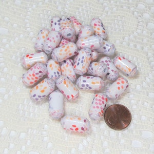 May include: A pile of white paper beads with orange, pink and purple polka dots. The beads are approximately 2.5 cm long and are arranged in a random pattern. A penny is included for scale.