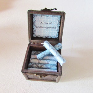 May include: A wooden box with a blue and gray patterned lid that says "A Box of Encouragement". The box is open and contains several rolled up pieces of paper with blue and gray patterned designs.
