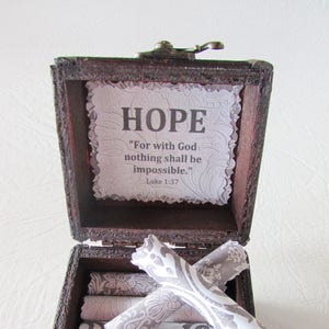 May include: A wooden box with a hinged lid, open to reveal a stack of rolled paper scrolls with a gray and white patterned design. The inside of the lid has a white card with the word "HOPE" in black lettering and the quote "For with God nothing shall be impossible." Luke 1:37.