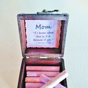 May include: A wooden box with a quote about love inside. The quote reads "If I know what love is, it is because of you." - Herman Hesse. The box is open and contains several rolled up pieces of paper.