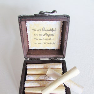 May include: A wooden box with a hinged lid and a small metal handle. The box is open and contains several rolled up pieces of paper with a floral design. The inside of the box lid has a message that reads "You are Beautiful, You are Magical, You are Capable, You are Wonderful."