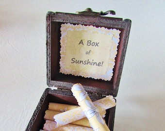 May include: A wooden box with a hinged lid and a brass latch. The box is open and contains several rolled up pieces of paper with a floral pattern. The lid has a label that reads "A Box of Sunshine!"