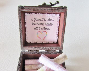 Pode incluir: Uma caixa de madeira com tampa de dobradiça, aberta para revelar um papel rosa com o texto "A friend is what the heart needs all the time." e um coração feito de corações coloridos. Dentro da caixa, há vários pedaços de papel rosa enrolados com padrões florais.