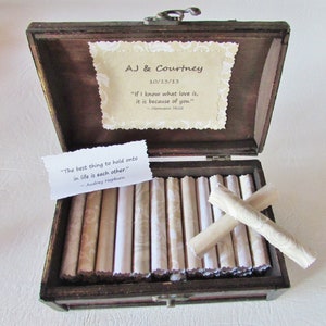 May include: A wooden box with a hinged lid, open to reveal a collection of rolled up papers inside. The box is decorated with a small card that reads "AJ & Courtney 10/13/13" and a quote by Hermann Hesse. Another card inside the box reads "The best thing to hold onto in life is each other." - Audrey Hepburn