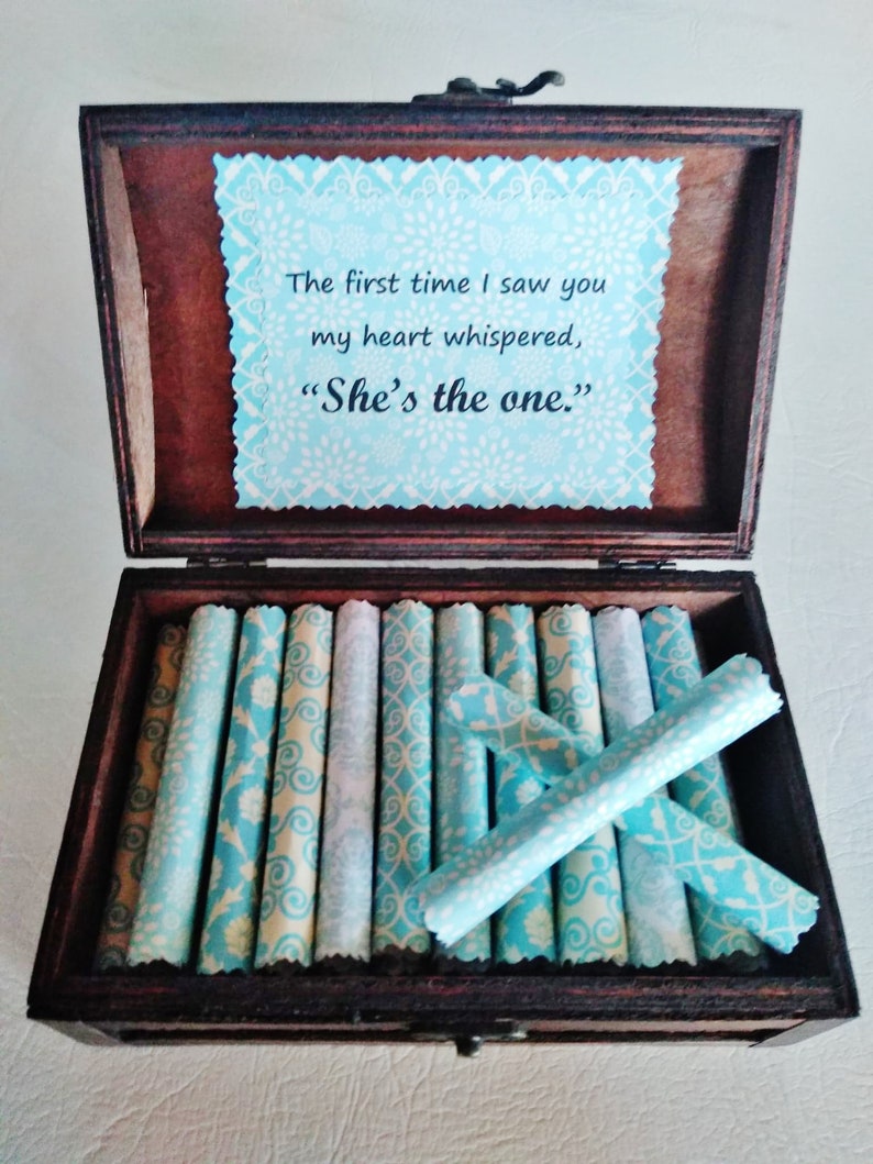May include: A wooden box with a blue and white patterned lid. The lid has a message that reads "The first time I saw you my heart whispered, 'She's the one.'" The box is filled with rolled up pieces of paper with a similar blue and white pattern.