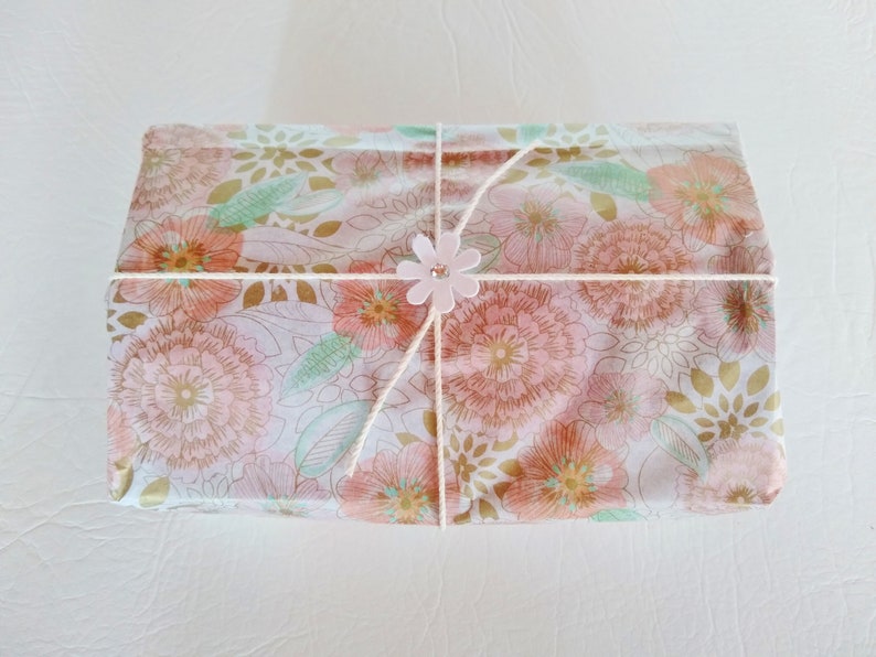 May include: A gift box wrapped in floral patterned paper with a pink flower embellishment tied with twine.