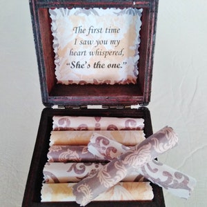 May include: A wooden box with a hinged lid, open to reveal a stack of rolled paper scrolls. The inside of the lid has a printed message that reads "The first time I saw you my heart whispered, "She's the one.""