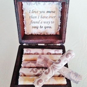 May include: A wooden box with a hinged lid, open to reveal a stack of rolled papers with a decorative pattern. The inside of the lid has a message that reads "I love you more than I have ever found a way to say to you."