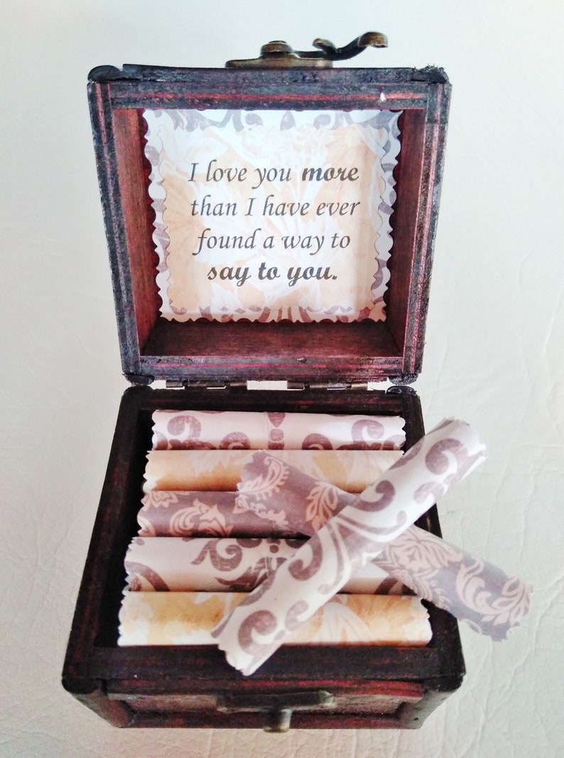 May include: A wooden box with a hinged lid, open to reveal a stack of rolled papers with a decorative pattern. The inside of the lid has a message that reads "I love you more than I have ever found a way to say to you."