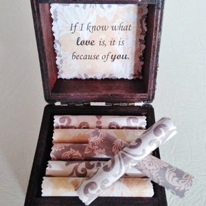 May include: A wooden box with a hinged lid and a brass latch. The box is open and contains several rolled pieces of paper with a floral pattern. The inside of the lid has a message that reads "If I know what love is, it is because of you."
