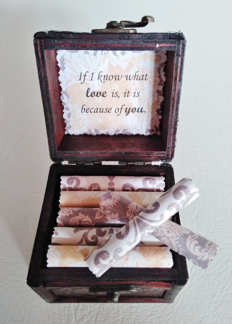 May include: A wooden box with a hinged lid and a brass latch. The box is open and contains several rolled pieces of paper with a floral pattern. The inside of the lid has a message that reads "If I know what love is, it is because of you."