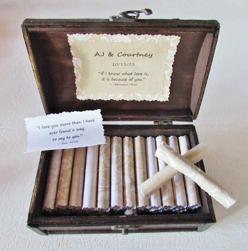 May include: A wooden box with a hinged lid, open to reveal a collection of rolled up papers. The box is decorated with a quote from Hermann Hesse: "If I know what love is, it is because of you." The box also includes a quote from Ben Folds: "I love you more than I have ever found a way to say to you."