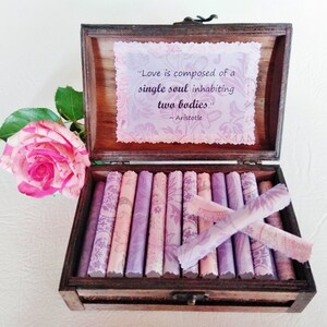 May include: A wooden box with a quote about love by Aristotle inside. The quote reads "Love is composed of a single soul inhabiting two bodies." The box is open and contains a stack of small, rolled-up pieces of paper with a floral pattern.