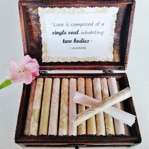 May include: A wooden box with a quote by Aristotle about love, "Love is composed of a single soul inhabiting two bodies." The box is open and contains several rolled up pieces of paper with a decorative pattern.
