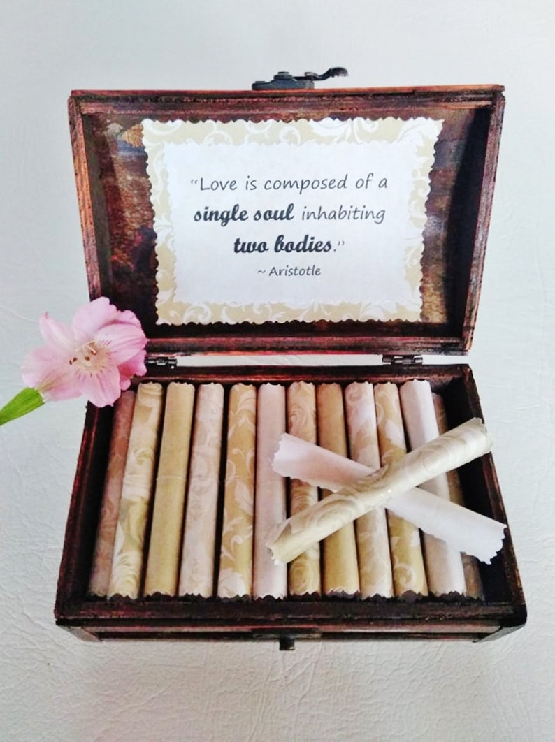May include: A wooden box with a quote by Aristotle about love, "Love is composed of a single soul inhabiting two bodies." The box is open and contains several rolled up pieces of paper with a decorative pattern.