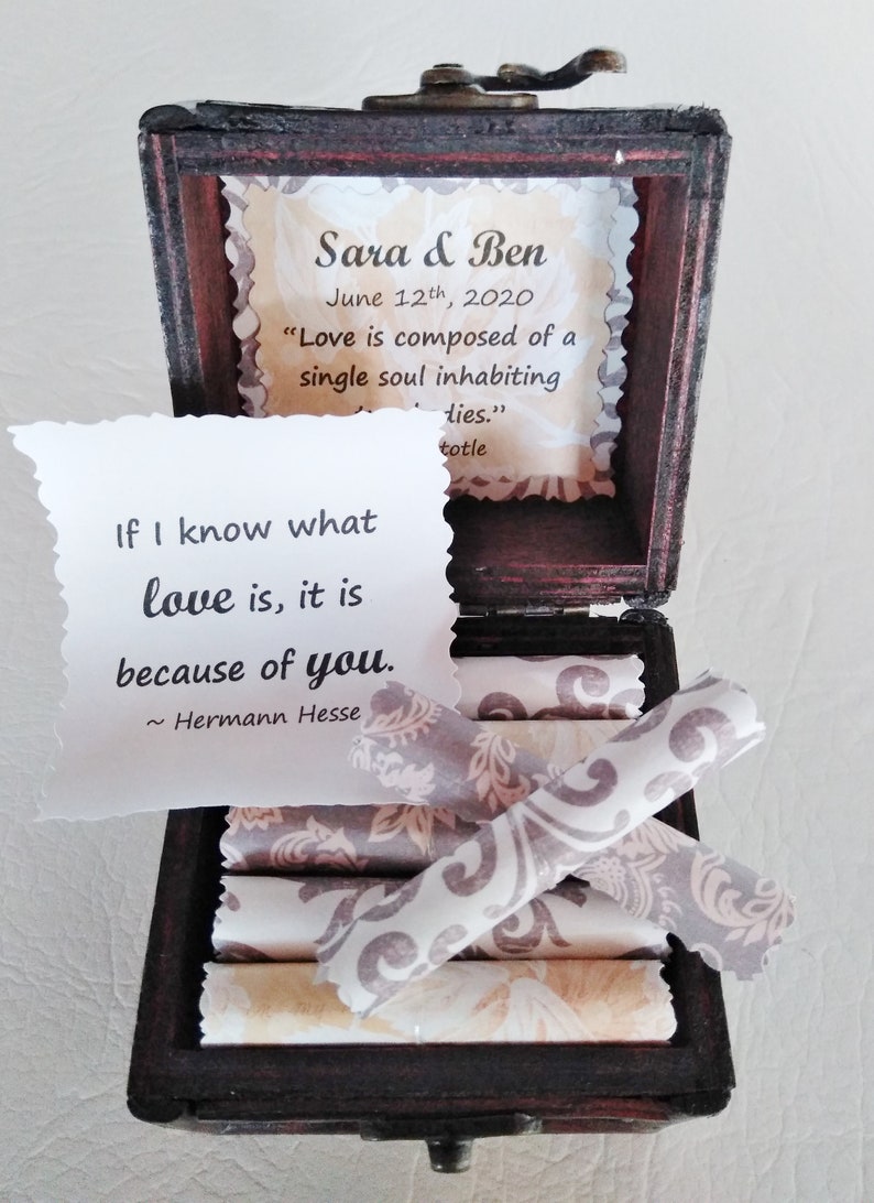 May include: A wooden box with a quote about love inside. The quote reads "If I know what love is, it is because of you." - Hermann Hesse. The box also has a small card inside with the names Sara & Ben and the date June 12th, 2020. The card also has a quote about love: "Love is composed of a single soul inhabiting two bodies." - Aristotle.