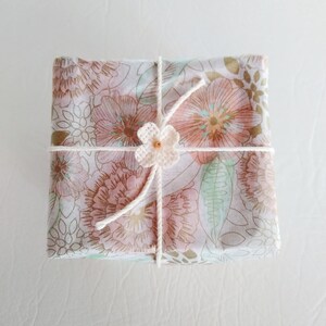 May include: A gift wrapped in white paper with a floral pattern. The paper is tied with white twine and a small white crocheted flower with a brown bead in the center.