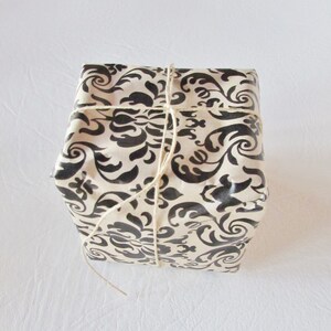 May include: A gift box wrapped in white paper with a black and white damask pattern. The box is tied with twine.