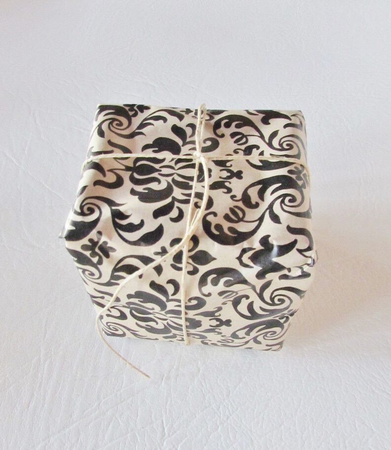 May include: A gift box wrapped in white paper with a black and white damask pattern. The box is tied with twine.