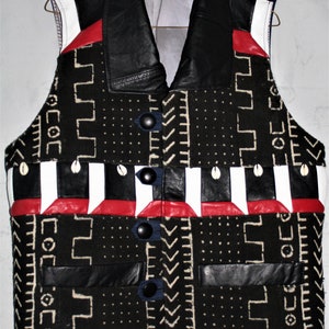 May include: A black leather vest with a white, red, and blue patterned fabric. The vest has a collar and a button closure. The fabric has a geometric pattern.