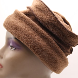 May include: A brown fleece hat with a layered design. The hat is made of a soft, textured material and features a darker brown trim along the edges. The hat is designed to be worn on the head.