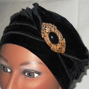 May include: A black velvet turban with a gold and black jeweled brooch.