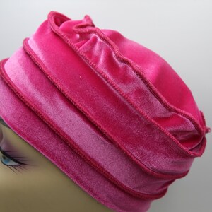 May include: A pink velvet hat with a ruffled edge. The hat is folded over itself several times, creating a layered effect.