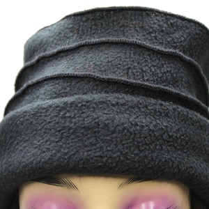 May include: A dark gray fleece hat with a rounded crown and three horizontal stitched bands. The hat has a soft, textured appearance and is designed to be worn on the head. The hat is a solid color and appears to be made of a warm material.
