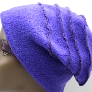 May include: A vibrant purple fleece beanie hat with a soft texture. The hat features decorative wavy stitching in a darker shade of purple. The hat is shown on a mannequin head.