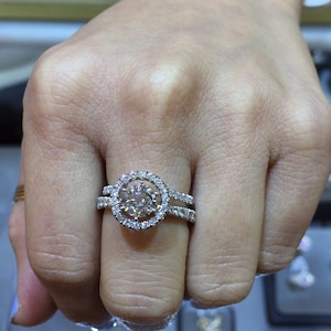 May include: A silver ring with a large round diamond surrounded by smaller diamonds. The ring has a double band.