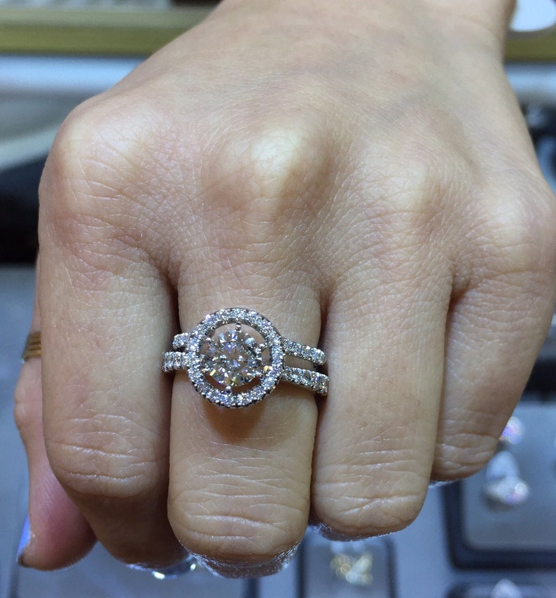 May include: A silver ring with a large round diamond surrounded by smaller diamonds. The ring has a double band.
