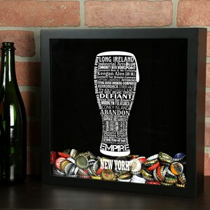 May include: A black framed shadow box with a white silhouette of a beer glass filled with the names of New York breweries. The glass is surrounded by a collection of colorful bottle caps.
