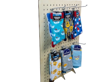 May include: A wooden pegboard display with hooks holding colorful socks with various patterns. The socks are packaged in plastic bags with labels that include the text "Men's" and "Fashion Socks Calzetterie De Style".