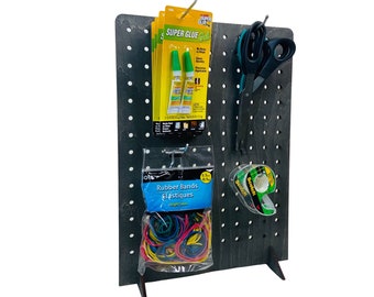 May include: A black pegboard with a stand, featuring various items including two tubes of super glue, a package of rubber bands, a roll of tape, and a pair of scissors.