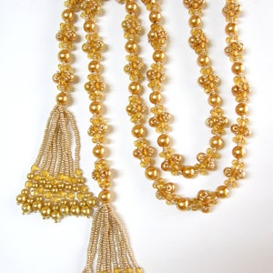May include: A long gold necklace with two tassels. The necklace is made of small gold beads and the tassels are made of smaller gold beads.