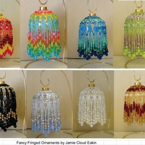 May include: Eight beaded Christmas ornaments with a fringed design. The ornaments are displayed on gold stands. The ornaments are in various colours, including red, yellow, green, blue, black, white, and gold.