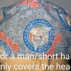 May include: A light blue surgical scrub cap with a repeating pattern of red and white text and blue circular emblems. The emblems feature a winged figure and the text "AERO FORCE ONE".