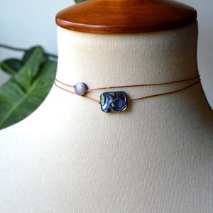 May include: A delicate choker necklace with two strands. One strand features a small, round, gray bead, and the other has a rectangular abalone shell pendant. The necklace is displayed on a mannequin.