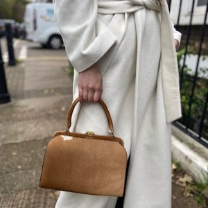 Könnte beinhalten: Eine braune und weiße Kuhfell-Handtasche mit einem goldenen Verschluss und einem oberen Griff. Die Tasche wird von einer Person in einem weißen Mantel gehalten.